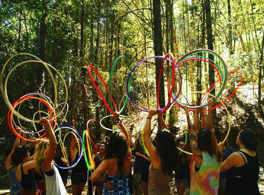 A circle of participants lifting colorful hoops together in the forest