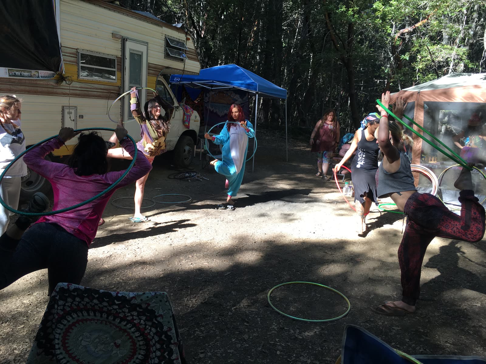 A circle of participants learning hoop movements in dappled sunlight