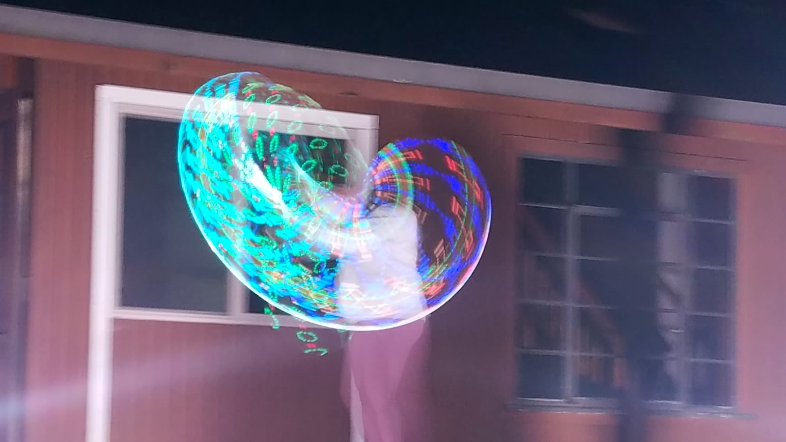 A performer surrounded by bright teal and multicolor LED hoop trails